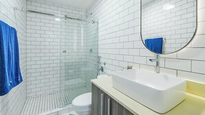 Ein modernes Badezimmer mit weißen, rechteckigen Fliesen, einer Duschkabine aus Glas, einem weißen Waschbecken und einem blauen Handtuch.