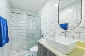 A modern bathroom with white subway tiles, a glass shower enclosure, a white sink, and a blue towel. - Casa Quijano 06 By Wynwood House (Panama City)