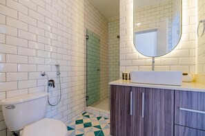 A bathroom with white subway tiles, a shower with a glass door, a toilet, and a vanity with a mirror. - Casa Quijano 06 By Wynwood House (Panama City)