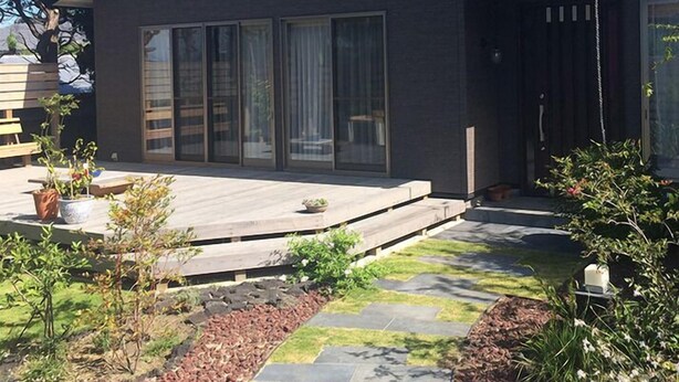 Una casa moderna con un amplio ventanal corredera, un patio y un jardín con plantas y un sendero de piedra.