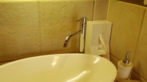 Un lavamanos blanco con grifo y jabonera, una caja de pañuelos y un dispensador de jabón sobre una encimera de madera.