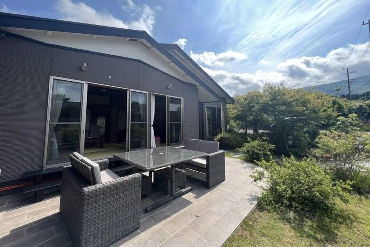 A modern house with a patio, large sliding glass doors, and a view of the surrounding greenery.