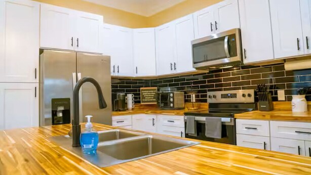 Una cocina moderna con armarios blancos, electrodomésticos de acero inoxidable y encimera de madera.