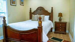 Un dormitorio con una cama de madera, una mesita de noche con una lámpara y dos cuadros en la pared.