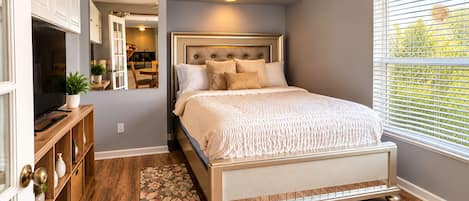 A bedroom with a bed, a ceiling fan, a window with blinds, and a wooden floor.