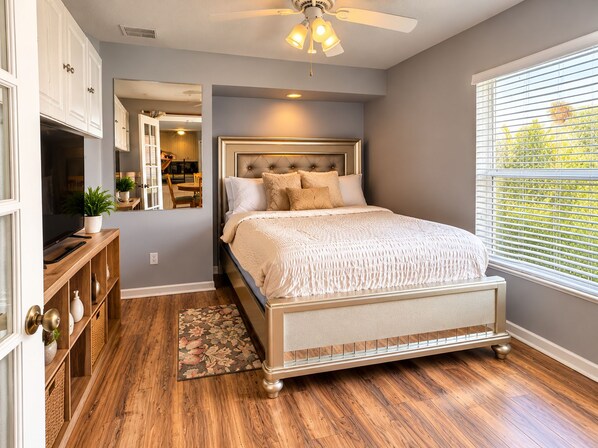 A bedroom with a bed, a ceiling fan, a window with blinds, and a wooden floor.
