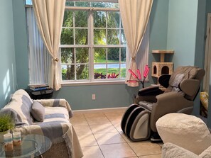 A room with a window, a massage chair, a cat tree, and a striped sofa.