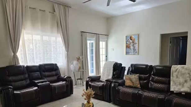 Una sala de estar con dos sofás de cuero negro, una mesa de centro de vidrio y un ventilador de techo.