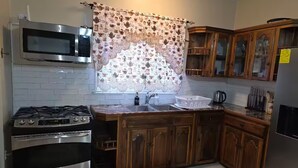 Cocina con estufa a gas, horno, microondas, gabinetes de madera y una ventana con cortinas estampadas.