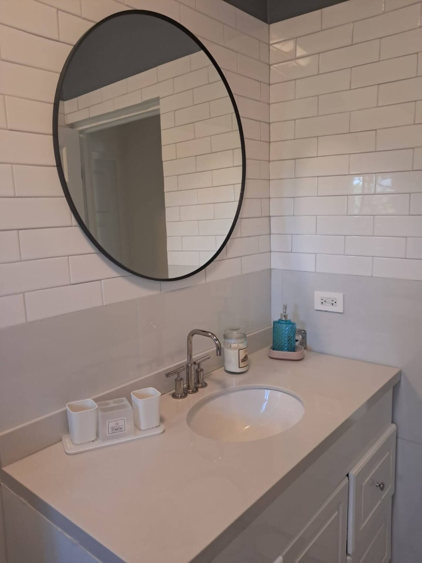 A bathroom with a white tiled wall, a round mirror, a sink with a faucet, and a small blue soap dish.