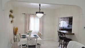 Un comedor con una mesa preparada para cuatro personas, una araña y una cocina visible a través de un arco.