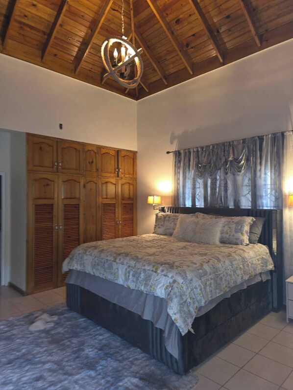Un dormitorio con techo de madera, cama con ropa de cama floral, armario y cortinas.