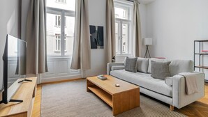 A modern living room with a sofa, coffee table, TV, and large windows with curtains. - Blueground | Innere Stadt, balcony, nr St. Stephen's Cathedral (Vienna)