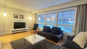 Olohuone, jossa on televisio, sohva, sohvapöytä ja suuret ikkunat.