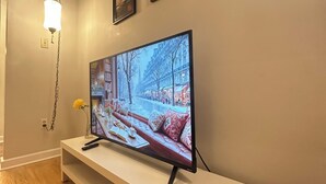 Moderni olohuone, jossa on valkoinen TV-taso, jossa on litteänäyttöinen televisio, riippuvalaisin sekä kaksi kehystettyä kuvaa seinällä.
