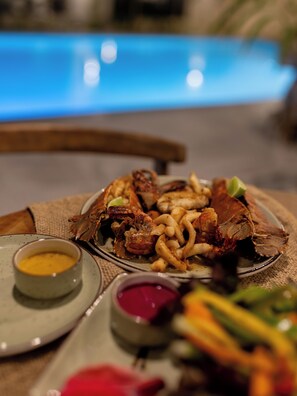 Una mesa de comedor con platos de mariscos, un tazón de sopa y una piscina al fondo.