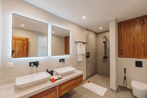 Une salle de bain moderne avec deux lavabos, un grand miroir, une douche et des meubles en bois.