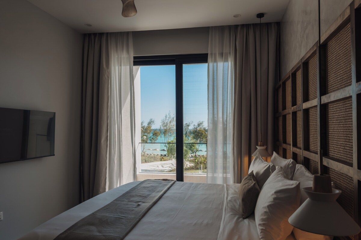 Un dormitorio con cama, cortinas, vistas al exterior y un televisor montado.