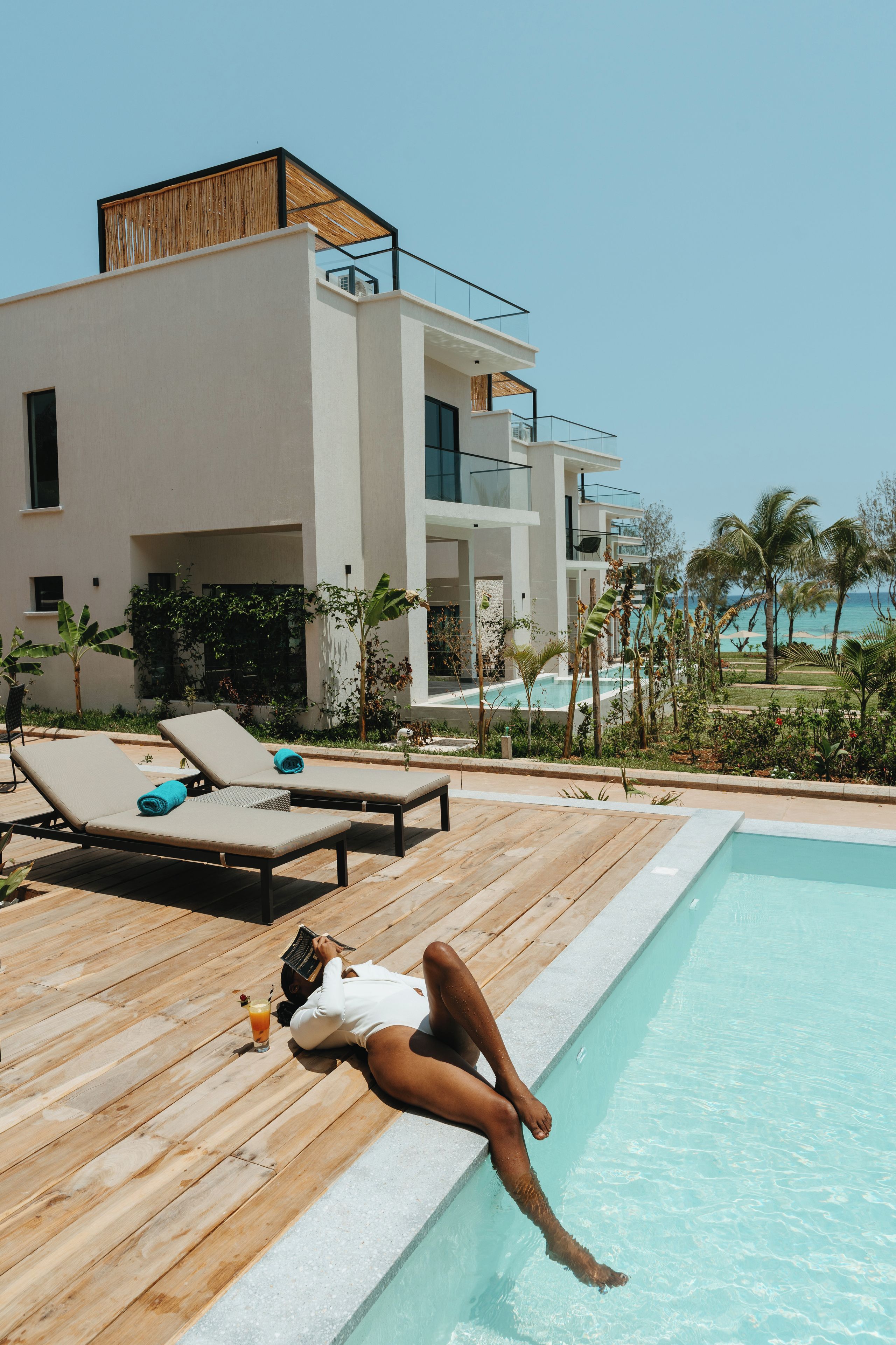 A modern building with a pool, lounge chairs, and a view of the ocean.