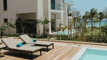 A modern building with a pool, lounge chairs, and a view of the ocean.