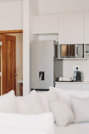 Una cocina moderna con gabinetes blancos, un refrigerador de acero inoxidable, un microondas y una cafetera.