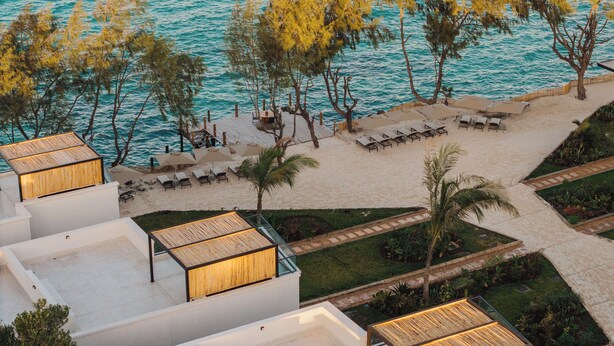 Un complexe hôtelier en bord de mer, doté de chaises longues, d’un espace piscine et offrant une vue sur la mer turquoise.