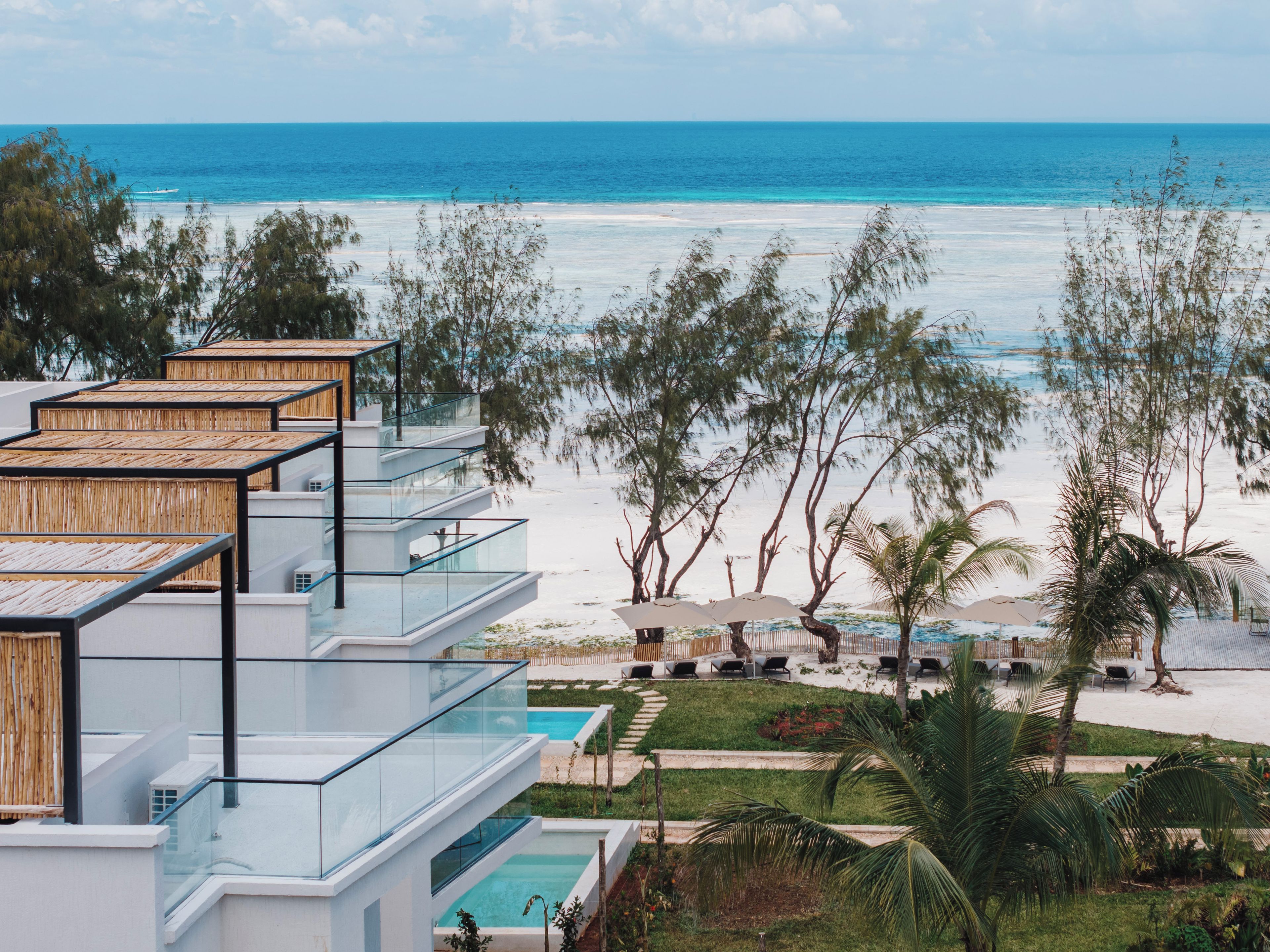 A beachfront hotel with multiple balconies overlooking the ocean, a pool area, and tropical landscaping.