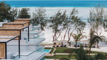 A beachfront hotel with multiple balconies overlooking the ocean, a pool area, and tropical landscaping.