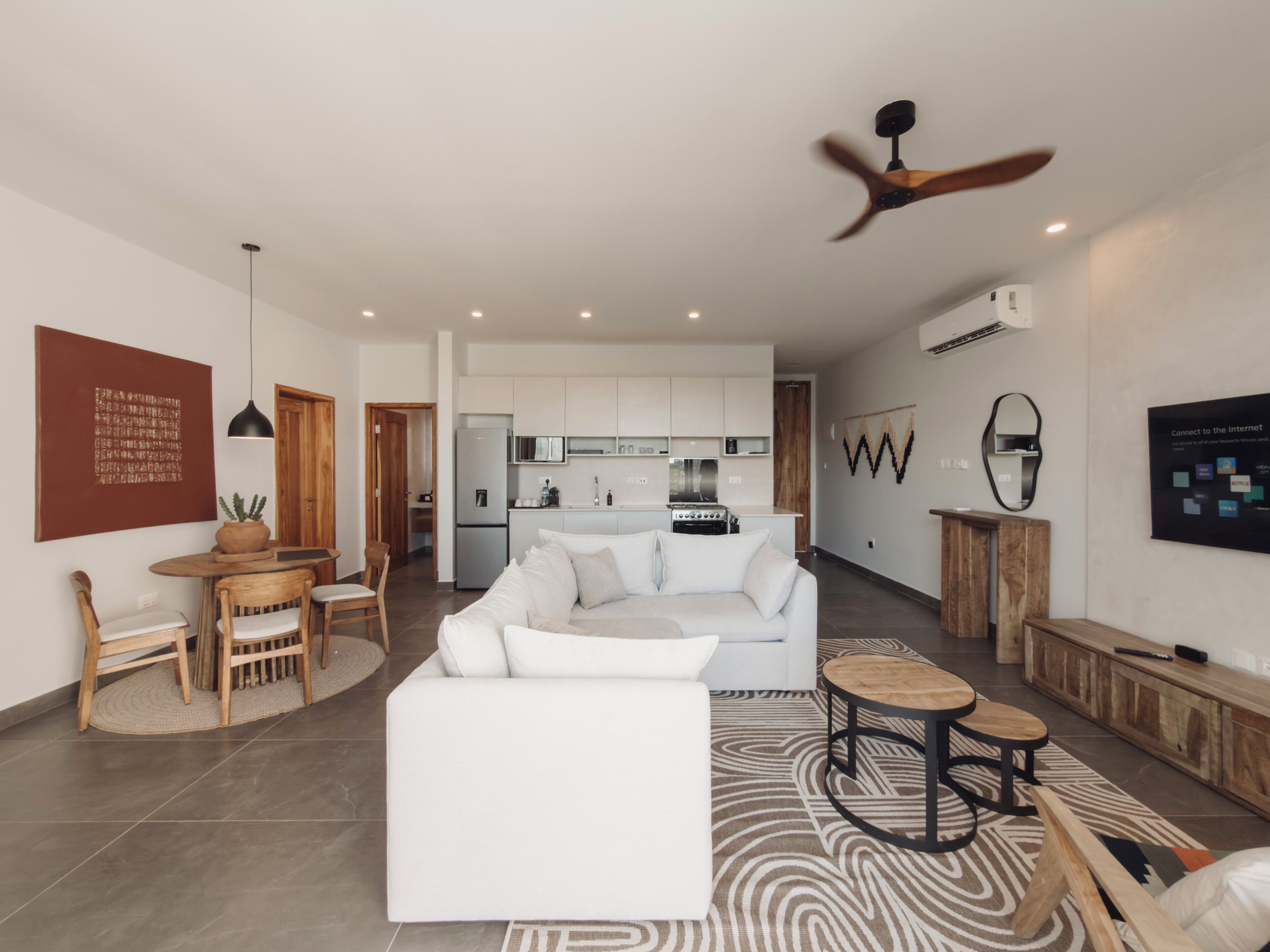 Una sala de estar moderna con un sofá blanco, una mesa de comedor de madera y una cocina al fondo.