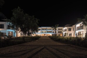 Un hotel moderno con un camino central que lleva a la entrada, rodeado de jardines cuidados y palmeras.