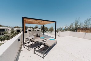 Una terraza en la azotea con una pérgola de madera, sillones de descanso y una mesa.