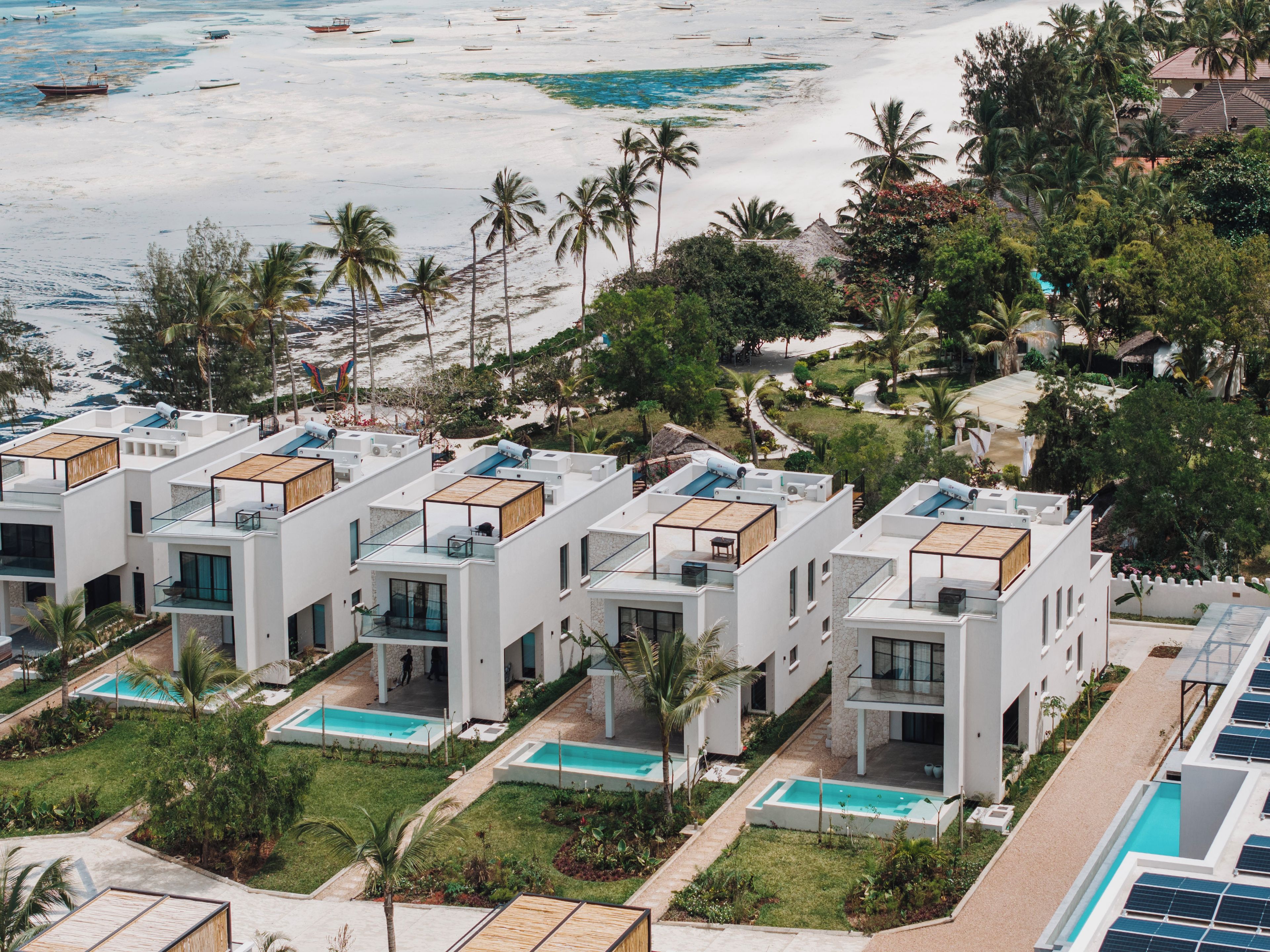 A modern resort with multiple white buildings, rooftop pools, and a beach view.