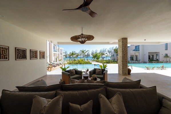 Una sala de estar moderna con un sofá grande, una mesa de centro y vistas a una piscina y palmeras.