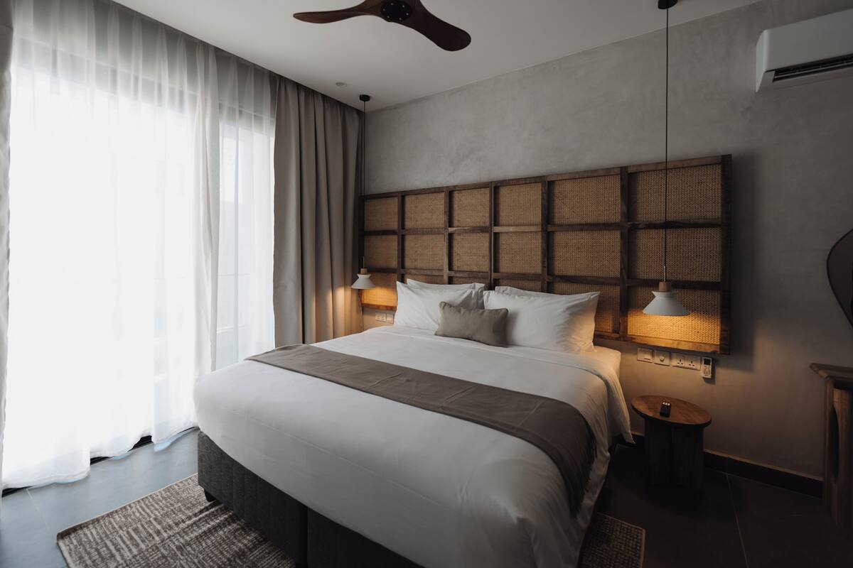 Une chambre d’hôtel moderne dotée d’un grand lit, d’un ventilateur de plafond, d’un téléviseur fixé au mur et d’une table de chevet avec une lampe.