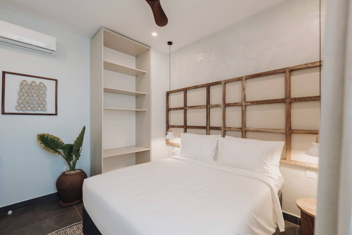 Une chambre avec un grand lit, des étagères intégrées, une plante en pot et un climatiseur fixé au mur.