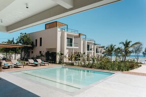 Un hotel moderno con piscina, sillas de descanso y vistas a la playa.