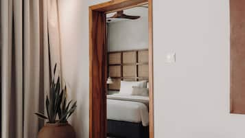 Quarto de hotel moderno com uma cama grande, porta de madeira que dá para um banheiro, uma planta em vaso e um espaço de refeições com mesa e cadeiras.