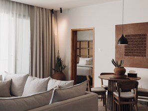 Un salon moderne comprenant un canapé, une table à manger avec des chaises, une plante en pot et un luminaire fixé au mur.