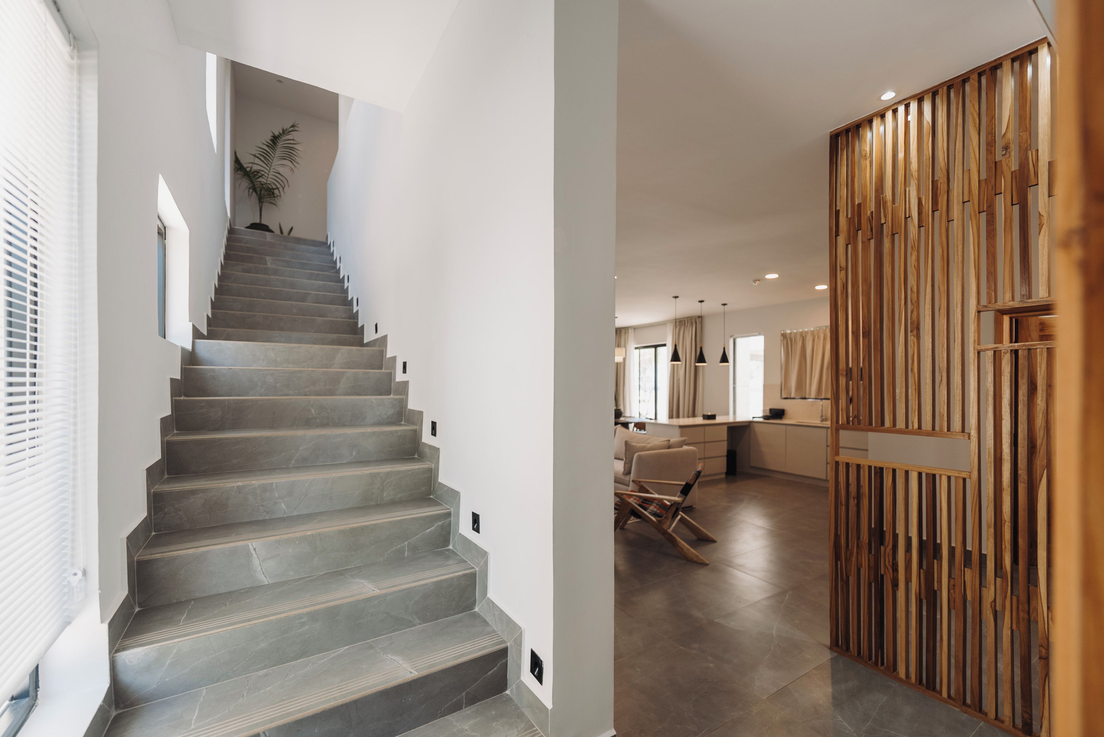 A staircase leading to a living area with a modern design, a wooden partition, and a dining area with a view.