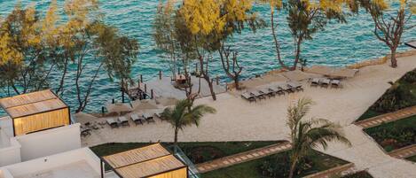 A beachside resort with sun loungers, a pool area, and a view of the turquoise sea.