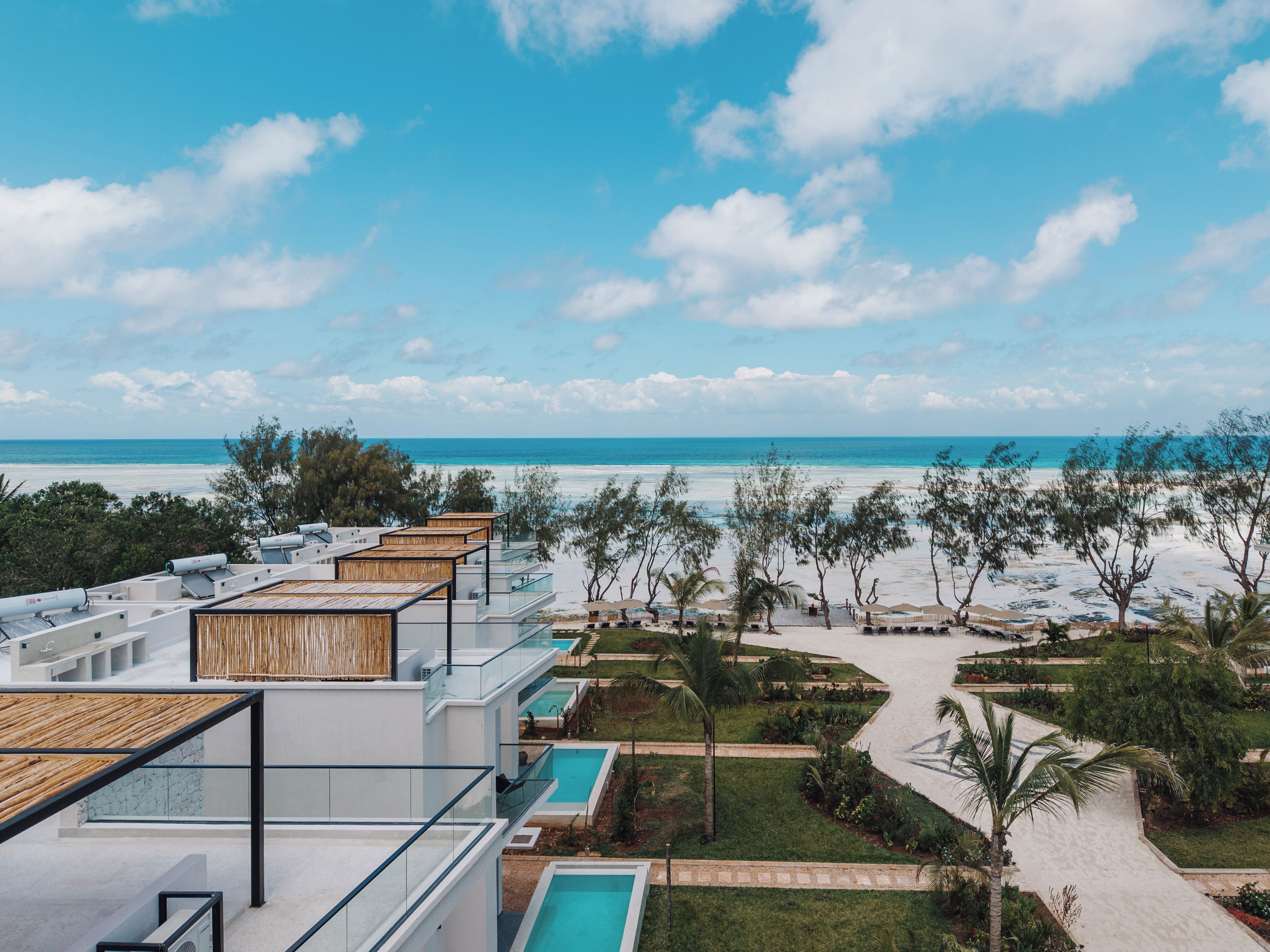 A modern resort with multiple swimming pools, a beach view, and a tropical garden.