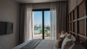 Une chambre à coucher avec un lit, des rideaux, une vue sur l’extérieur et un téléviseur fixé au mur.
