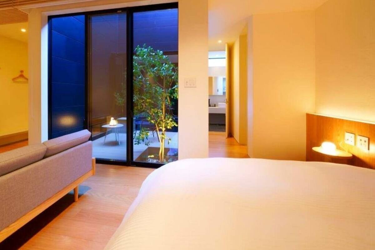 Ein modernes Hotelzimmer mit einem großen Bett, einer Couch, einer Schiebetür zu einem Balkon und einem kleinen Tisch mit einer Lampe.