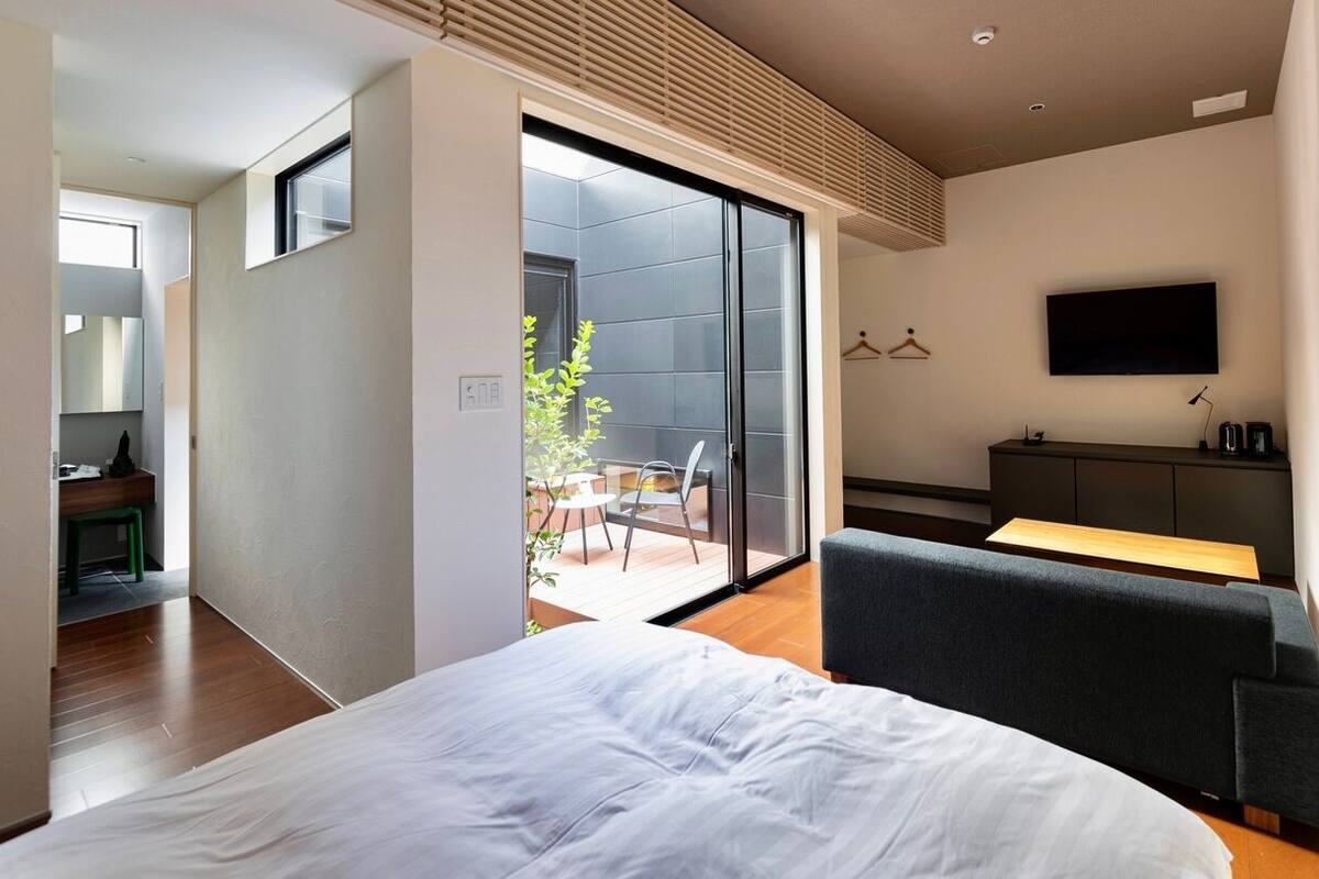 Ein modernes Hotelzimmer mit einem großen Bett, einem Fernseher, einem Balkon mit Essbereich und einer Schiebetür zu einer Terrasse.