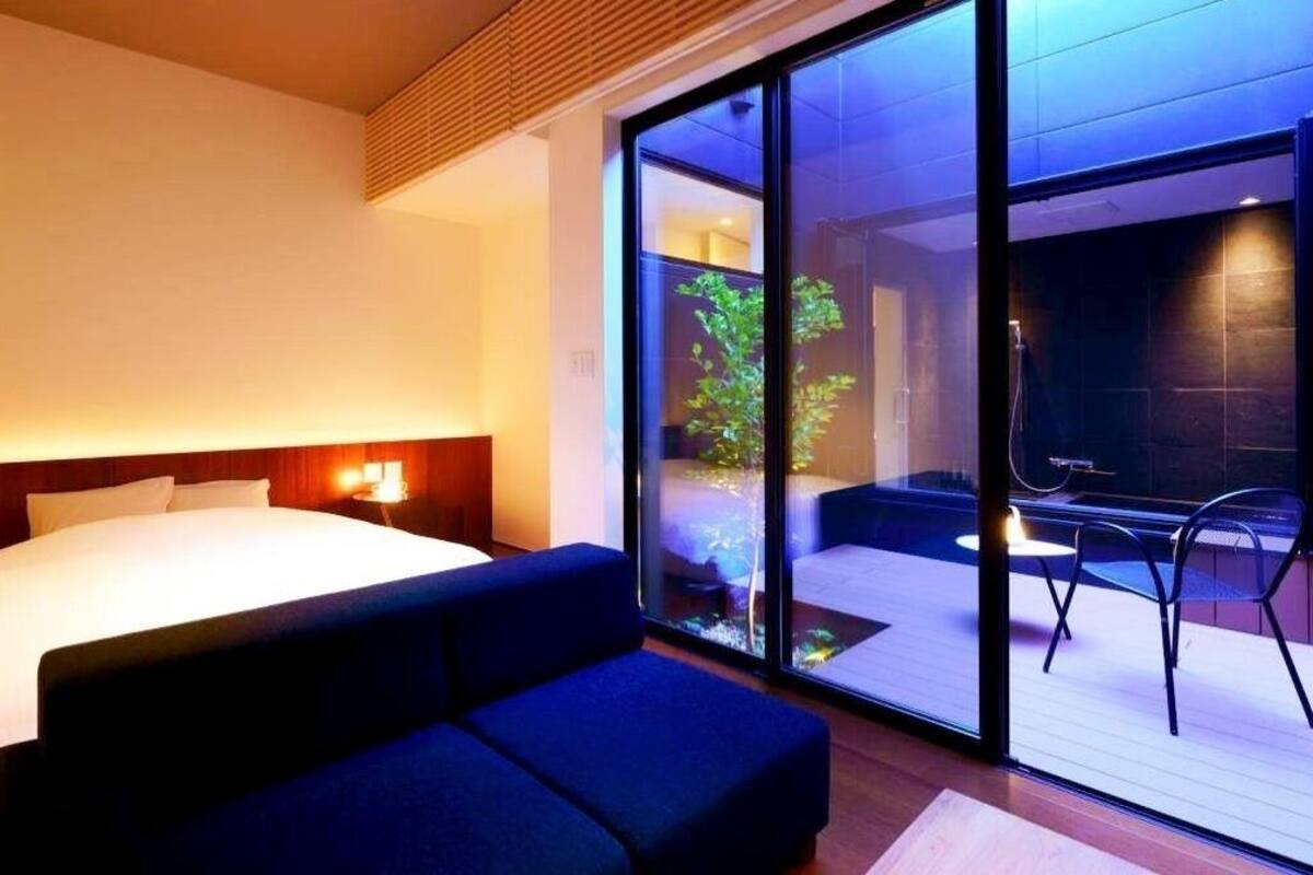 Ein modernes Hotelzimmer mit einem großen Bett, einer Couch und einer Glastür, die zu einem Außenbereich mit Tisch und Stühlen führt.