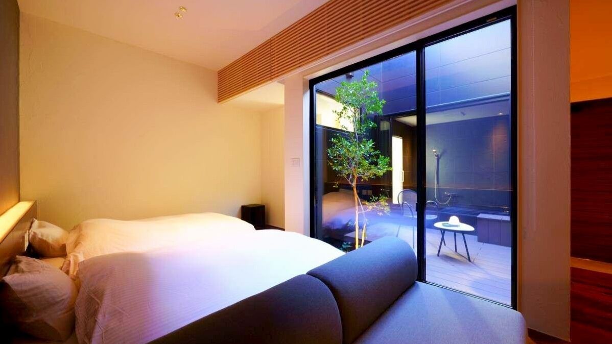 A modern hotel room with a bed, a small table, and a view of an outdoor deck.