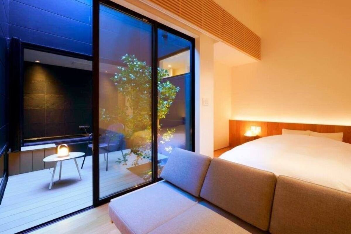 Ein modernes Hotelzimmer mit einem großen Bett, einer Sitzecke und einer Glasdoor, die zu einem Außenbereich führt.