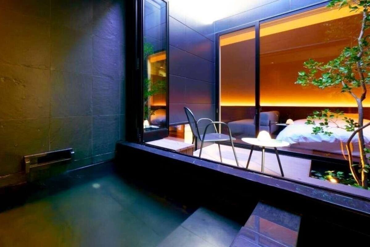 Ein modernes Hotelzimmer mit Glastrennwand, einer kleinen Sitzecke und einem sichtbaren Bett.