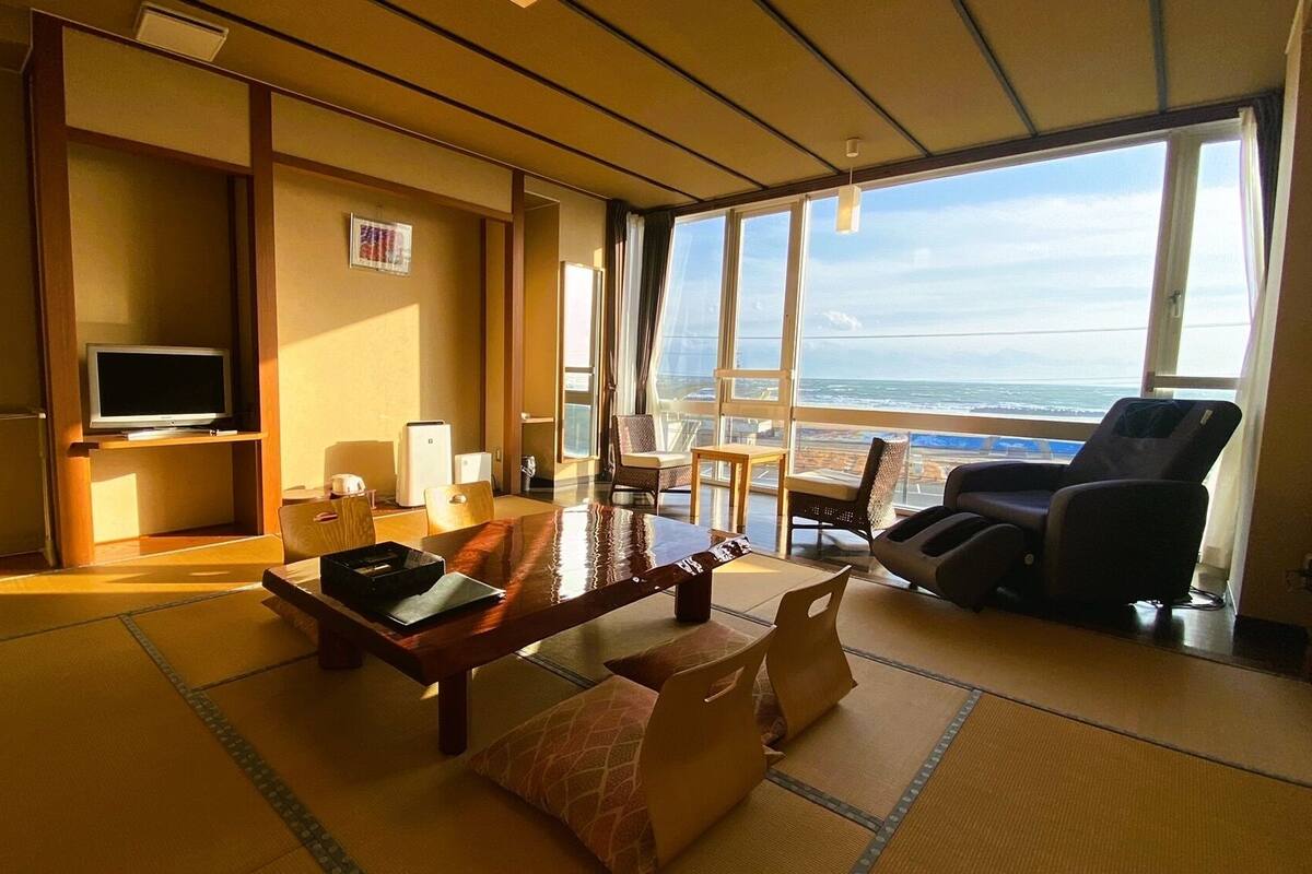 Una habitación con suelo de tatami, televisión, escritorio, silla y sillón de masaje.