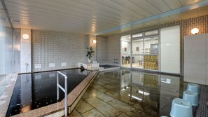 Ein moderner, überdachter Schwimmbereich mit klarer Wasserfläche, einer Sitzgelegenheit mit einer Bank und einer Wand mit einem gemusterten Design.